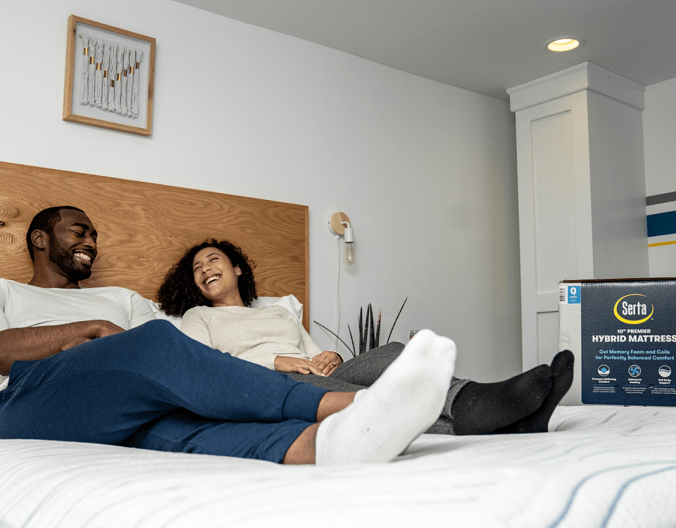 Couple sitting on bed with Serta box in corner